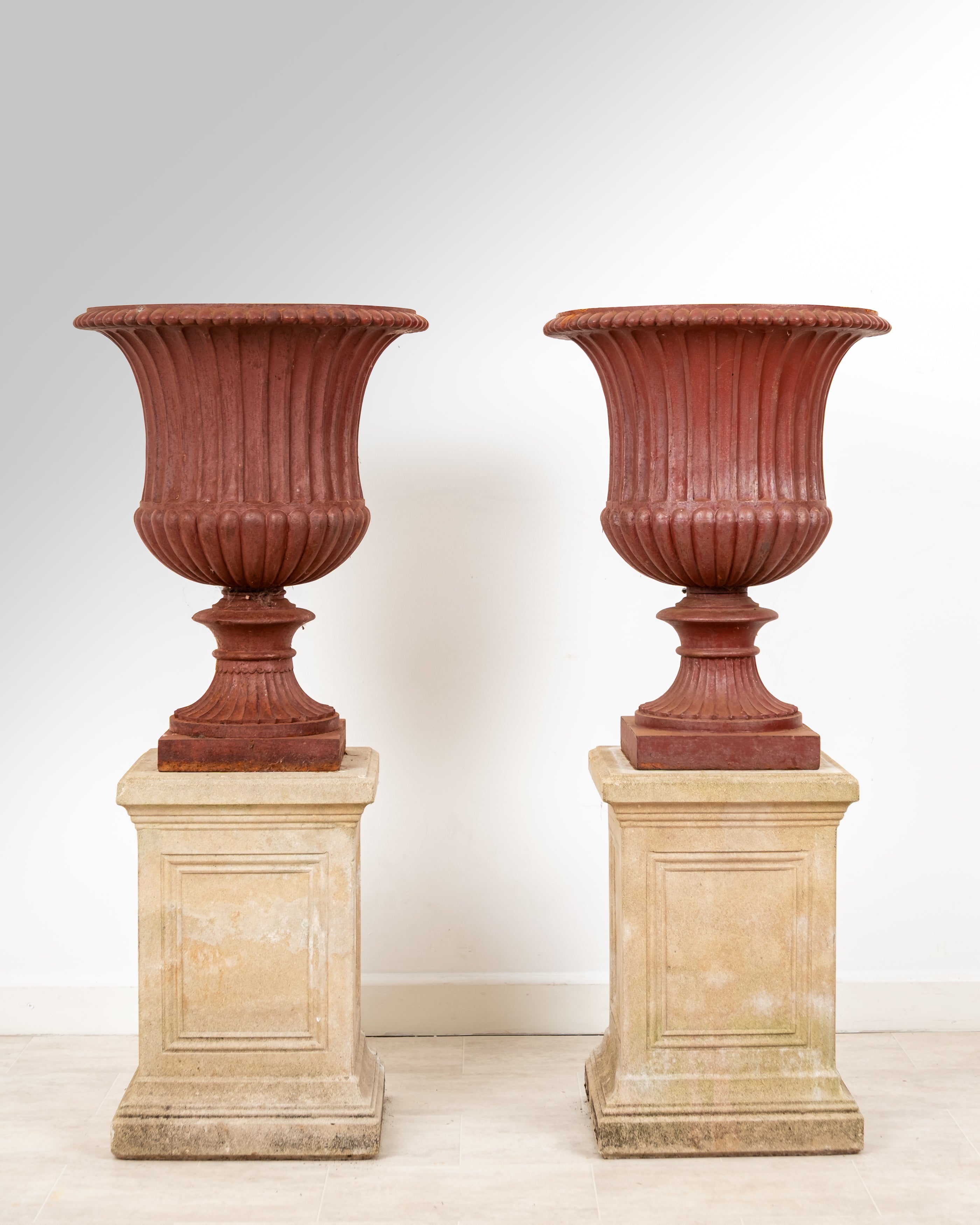 Pair of antique cast iron Campana garden urns on stone pedestals